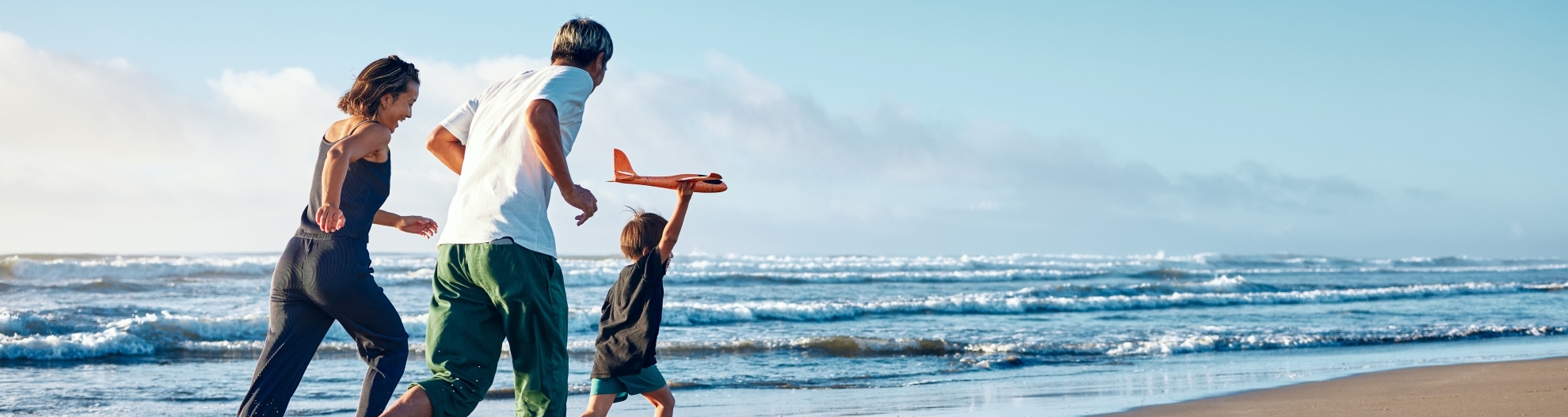 Parents running behind a boy running straight ahead with a model airplane held high in one hand